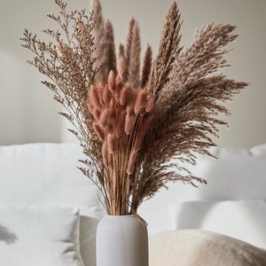 Op de afbeelding: Een witte keramische vaas gevuld met gedroogd pampasgras, konijnenstaarten en andere gedroogde grassen. De vaas staat op een houten tafel. Ook verkrijgbaar: Bruin Pampas-Set. Link in de beschrijving.