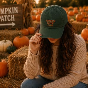Könnte beinhalten: Eine dunkelgrüne Baseballkappe mit dem gestickten Text PUMPKIN PATCH CLUB in orangefarbenen Buchstaben auf der Vorderseite. Die Kappe hat einen gebogenen Schirm und eine strukturierte Krone aus festem Stoff mit sichtbaren Nähten.