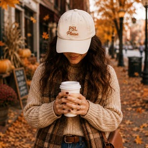 May include: A cream-colored baseball cap with the text PSL Please embroidered in brown on the front. The cap features a curved brim and a structured crown, providing a classic look. It is made of fabric and is designed to be worn on the head.