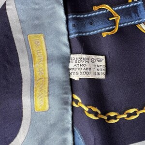 May include: A blue and white silk scarf with a gold chain and belt buckle design. The scarf has a label that reads '100% SILK - KENZO - DRY CLEAN ONLY - MADE IN FRANCE'.