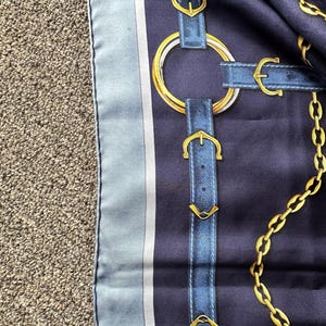 May include: A blue and white silk scarf with a pattern of gold chains and blue leather straps with gold buckles.