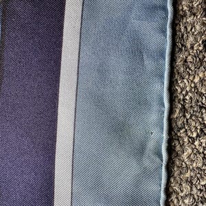 May include: A close-up of a blue and white striped fabric with a white border. The fabric has a subtle texture and a slight sheen.