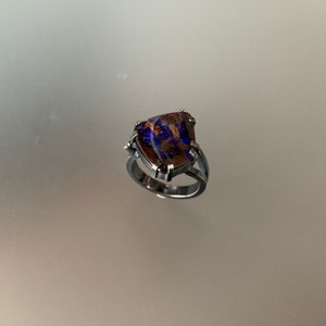 May include: A silver ring with a large, triangular, iridescent opal gemstone set in a prong setting. The opal has shades of purple, blue, and brown.