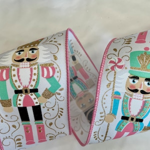 May include: White ribbon with a pink trim featuring a repeating pattern of nutcracker figures in pink, green, and blue with gold accents. The nutcrackers are holding candy canes and other festive items.