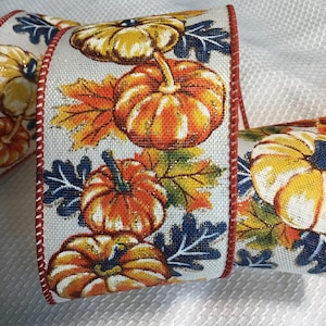May include: White ribbon with a fall theme featuring orange and yellow pumpkins with blue and green leaves. The ribbon has a red and white trim.