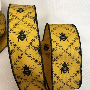 Op de afbeelding: Geel lint met een zwarte rand en een herhalend patroon van zwarte bijen en bladeren.