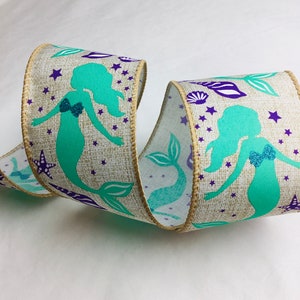 May include: A teal and purple ribbon with a mermaid design on a burlap background. The ribbon features mermaids, seashells, and stars.