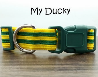 May include: A green and yellow striped dog collar with a silver D-ring and a green plastic buckle. The collar has the text "My Ducky" printed on it.