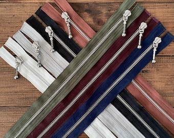 May include: A collection of eight different zipper closures with silver metal teeth and sliders. The zippers are in various colours, including black, white, brown, red, and green.
