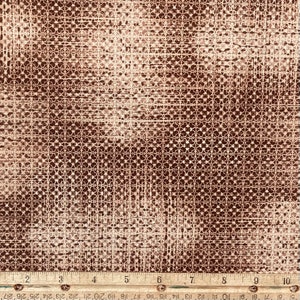 Peut inclure: Gros plan sur un tissu texturé avec un motif répétitif de petites formes interconnectées. Le tissu présente un mélange de tons bruns et beiges, créant un effet subtil et moucheté. Une règle est en bas de l'image, indiquant les centimètres.