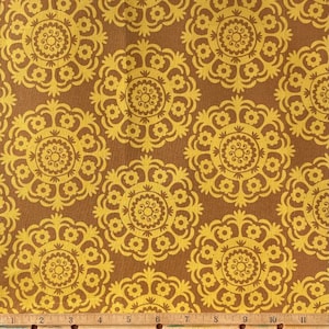 Peut inclure: Un tissu brun avec un motif répétitif de médaillons floraux stylisés jaunes. Le tissu est mesuré avec une règle en pouces.