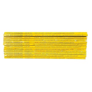 May include: A stack of National Geographic magazines with yellow covers. The magazines are from various months in 2002, with titles visible on the spines. The text includes topics like the Inca, Afghanistan, and the Great Lakes.