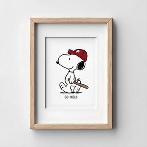Può includere: Una stampa incorniciata raffigurante un cane dei cartoni animati che indossa un berretto da baseball rosso con una P bianca e tiene in mano una mazza da baseball marrone. Il personaggio cammina e il testo GO PHILS è stampato in nero. Cornice in legno chiaro.
