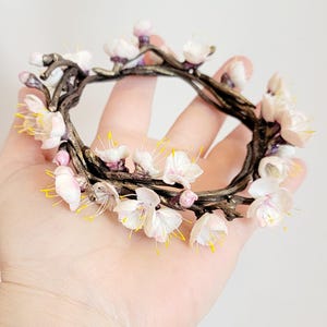 Può includere: Una delicata corona floreale realizzata con fiori bianchi e rosa con centri gialli. La corona è realizzata in filo metallico e ha la forma di un cerchio. È un gioiello bellissimo e unico.