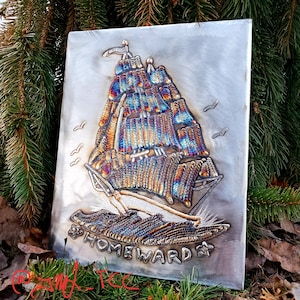 May include: A metal wall art piece depicting a ship with sails, with the word "HOMEWARD" below it. The ship is made of welded metal and has a rainbow-like iridescent finish.