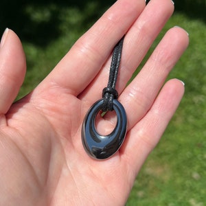 May include: A black oval pendant with a ring in the center, hanging from a black cord.