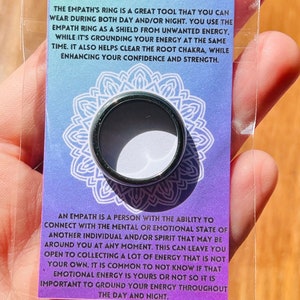 May include: A silver ring with the text "The Empath's Ring" on a card with a purple and blue background. The text on the card explains that the ring is a tool to help empaths ground their energy and enhance their confidence and strength.