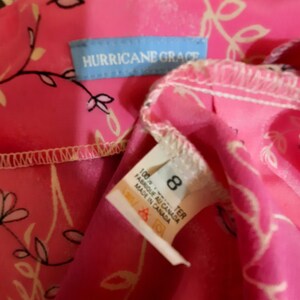 May include: Pink and white floral print dress with a blue tag that says "Hurricane Grace". The tag also includes size 8 and care instructions. The dress is made in Canada.