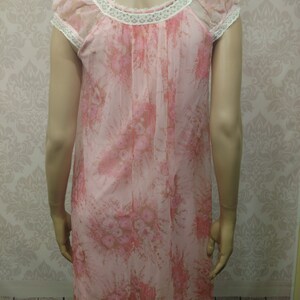 Pode incluir: Uma camisola de noite vintage rosa floral com mangas curtas e decote redondo adornado com renda branca. O tecido transparente apresenta um delicado padr&atilde;o floral em tons de rosa e castanho. Um estilo cl&aacute;ssico e feminino.