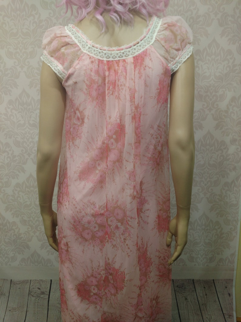 Pode incluir: Uma camisola de noite vintage rosa floral com mangas curtas e decote redondo adornado com renda branca. O tecido transparente apresenta um delicado padr&atilde;o floral em tons de rosa e castanho. Um estilo cl&aacute;ssico e feminino.