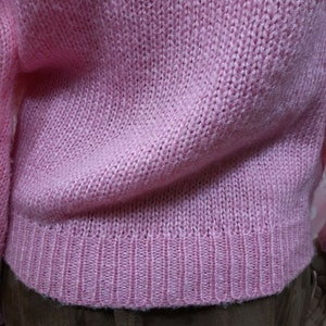 May include: A pink knitted sweater with a ribbed hem.