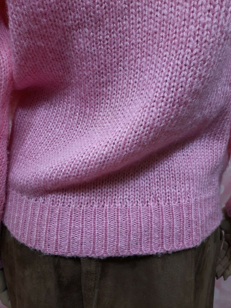 May include: A pink knitted sweater with a ribbed hem.