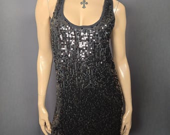 May include: A black sequin tank dress with a scoop neckline. The dress is sleeveless and has a mini length. A beaded necklace with a cross pendant is worn with the dress. The dress is displayed on a mannequin.