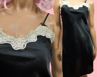May include: A black satin slip dress with a white lace trim around the neckline. The dress has thin straps and a straight silhouette.