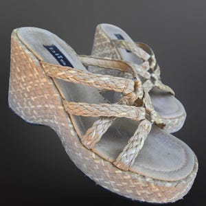 May include: Beige wedge sandals featuring woven raffia platforms and straps. The sandals have a braided design on the straps and a basket-weave pattern on the platform. The brand name "bliss" is visible on the inner sole.