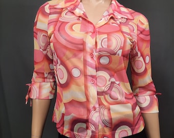 May include: A pink and orange long-sleeved shirt with a geometric pattern. The shirt has a button-up front and a collar.
