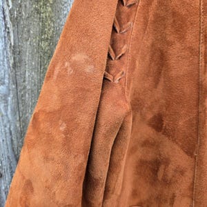 May include: A brown suede jacket with a laced detail on the sleeve.
