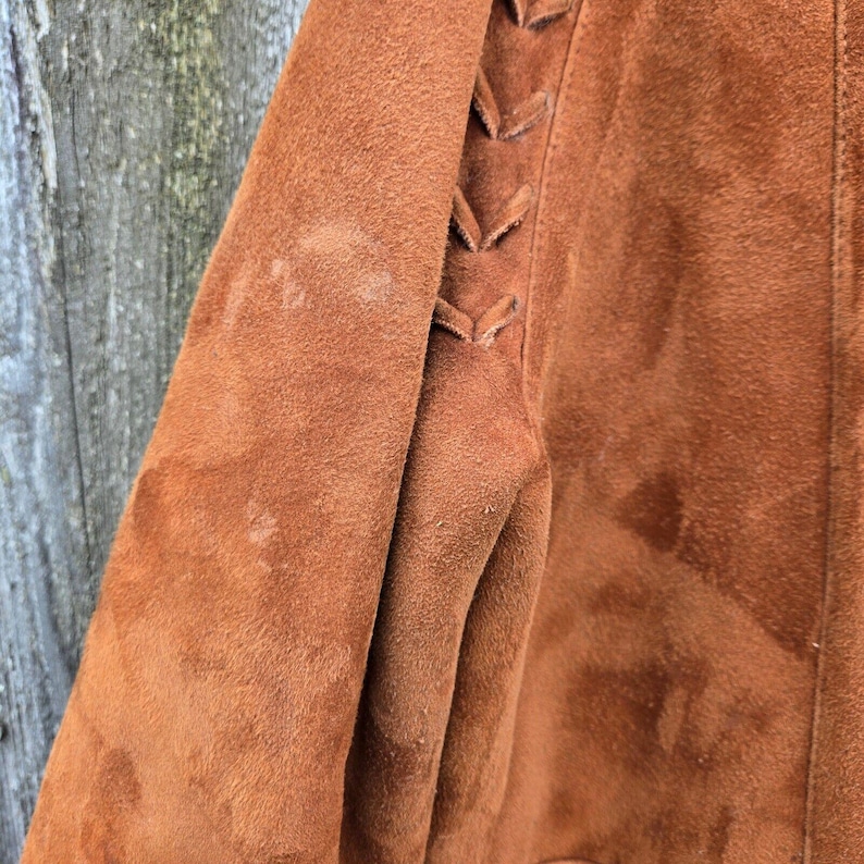 May include: A brown suede jacket with a laced detail on the sleeve.