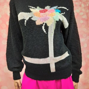 May include: Black sweater with a white and colorful floral design. The sweater has long sleeves and a crew neck.