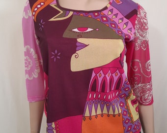 May include: A long-sleeved shirt with a colorful abstract design featuring a face with a large eye and geometric shapes. The shirt is made of a sheer fabric with a pink and purple color scheme.