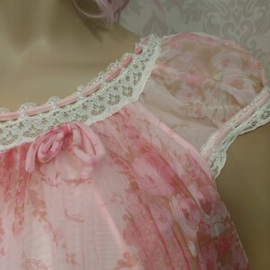 Pode incluir: Camisa de dormir rosa claro com um padr&atilde;o floral. A camisa de dormir apresenta uma delicada renda ao longo do decote e das mangas, com pequenos bot&otilde;es rosa e um la&ccedil;o. As mangas s&atilde;o transparentes e o tecido &eacute; leve.