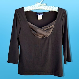 May include: A black long-sleeved shirt with a satin neckline. The neckline has a criss-cross design and is a darker shade of brown.