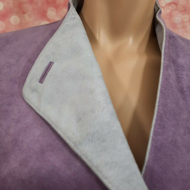 May include: A purple suede jacket with a light gray suede lining. The jacket has a V-neck and a single button closure.
