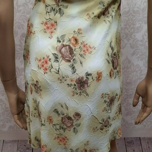 May include: A yellow floral dress with a white background. The dress has a fitted bodice and a flowing skirt. The floral pattern is made up of roses, leaves, and other small flowers.