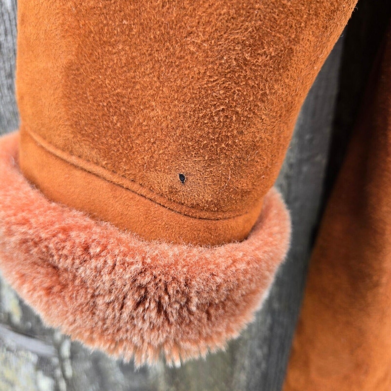 May include: Close-up of a brown suede jacket with a brown fur collar. The jacket has a small dark spot on the suede.