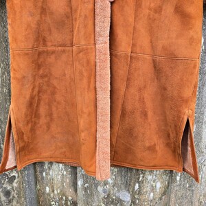 May include: Close-up of a brown suede jacket with a fuzzy brown lining. The jacket has a seam down the center front and two side slits.