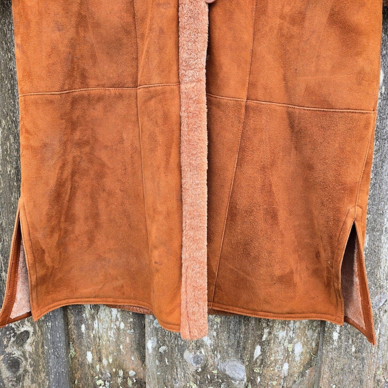 May include: Close-up of a brown suede jacket with a fuzzy brown lining. The jacket has a seam down the center front and two side slits.