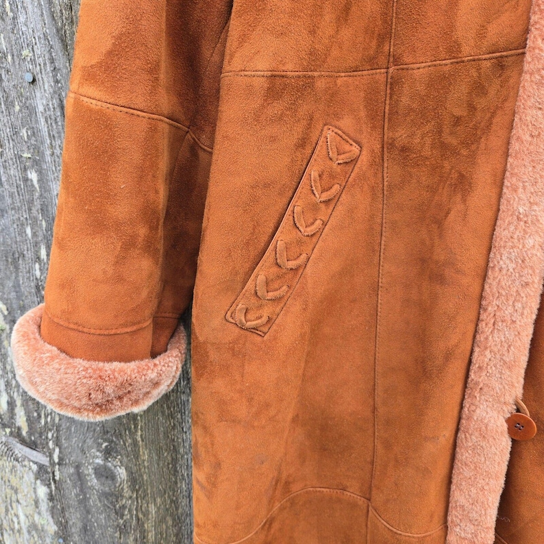 May include: A brown suede coat with a shearling lining and a decorative braided detail on the pocket.