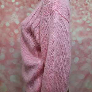 May include: A pink knitted sweater with a cable knit pattern. The sweater has a high neck and long sleeves.