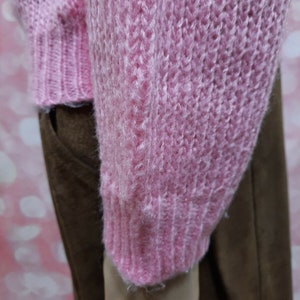 May include: A pink fuzzy knit sweater with a ribbed texture. The sweater is shown on a mannequin wearing brown pants.