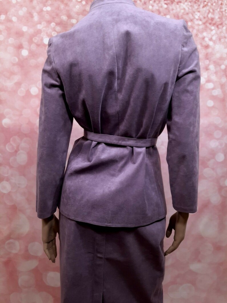 May include: A purple suede skirt suit with a matching jacket and skirt. The jacket has a belt and a stand-up collar.
