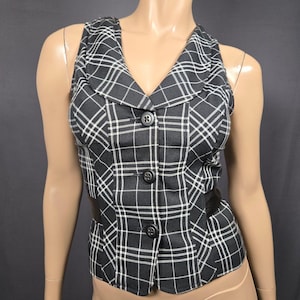 May include: A black and white plaid vest with a notched collar and three black buttons. The vest has a fitted silhouette and a black band at the waist. The plaid pattern features white lines on a black background.