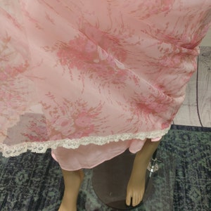 Pode incluir: Camisa de noite vintage rosa claro com um padr&atilde;o floral em tons de rosa e castanho. A camisa de noite tem uma delicada renda na bainha. A pe&ccedil;a de roupa &eacute; exibida num manequim.