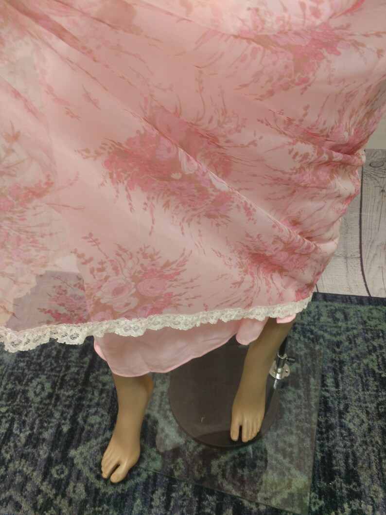 Pode incluir: Camisa de noite vintage rosa claro com um padr&atilde;o floral em tons de rosa e castanho. A camisa de noite tem uma delicada renda na bainha. A pe&ccedil;a de roupa &eacute; exibida num manequim.