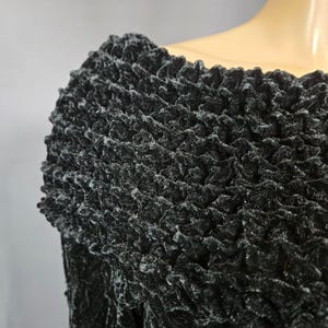 May include: Black off-the-shoulder sweater with a textured, crinkled fabric.