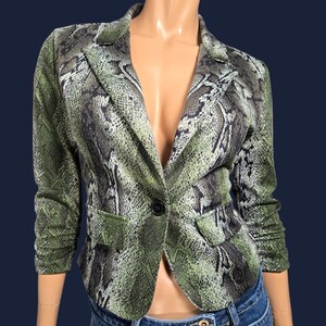 Peut inclure: Blazer vert et noir à motif peau de serpent, avec une fermeture à bouton noir unique. Le blazer a des manches trois-quarts et deux poches avant. Le vêtement est présenté sur un mannequin.